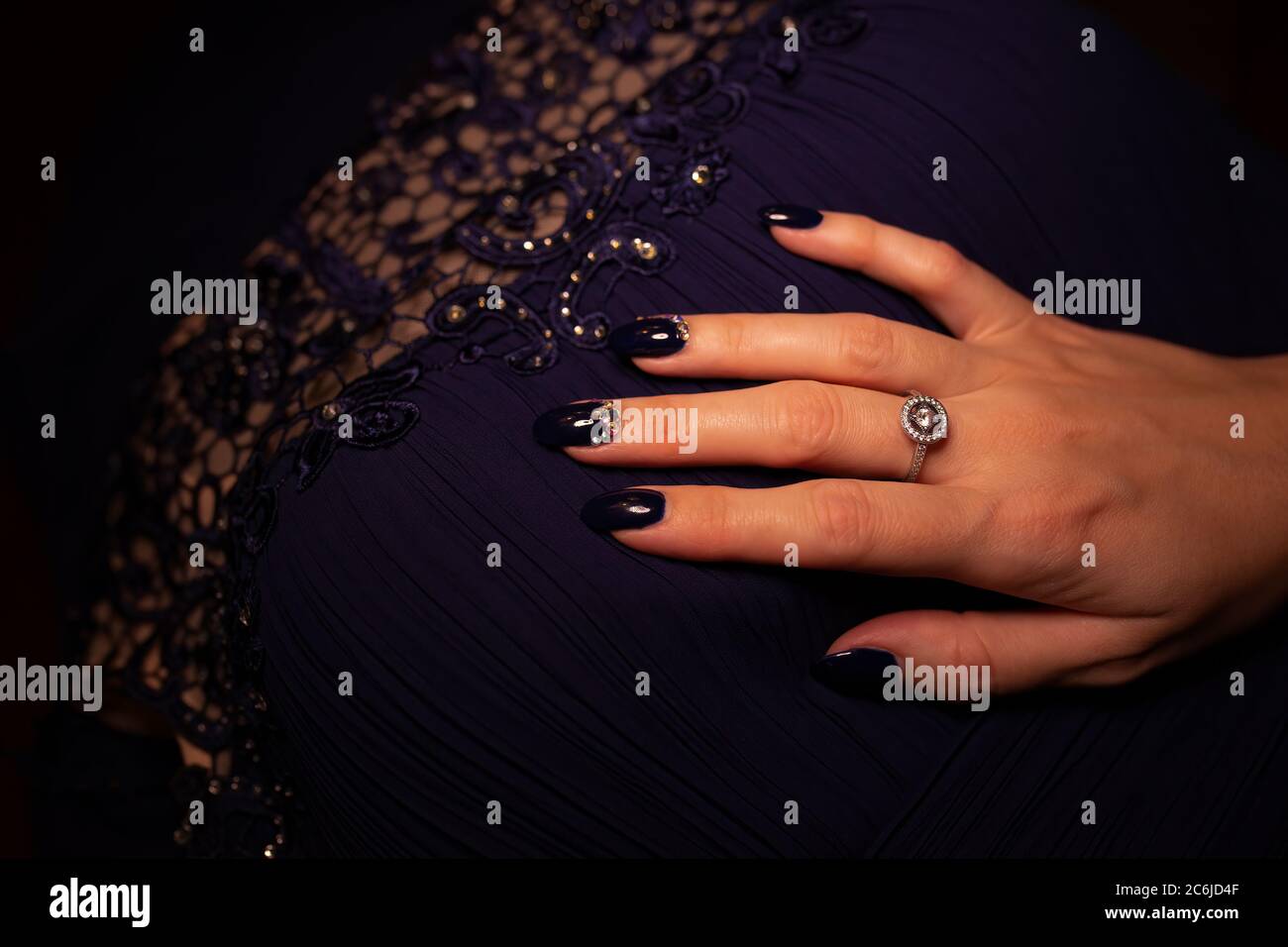Young Woman`s hand with long blue manicure resting on matching evening dress Stock Photo